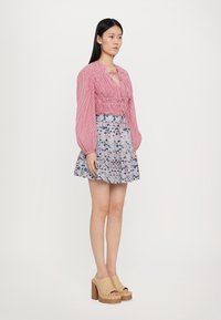 Rosa stripete croppede bluse med smockdetalj, kombinert med et floralmønstret skjørt. Modellen har på seg beige åpne platåsko.