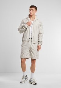 Leichte beige Windjacke mit hohem Kragen, kombiniert mit passenden Shorts. Verfügt über subtile Nähte und ein lässiges Design.