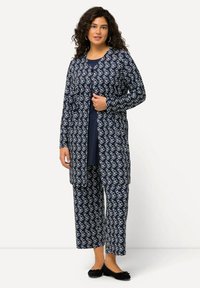 Marineblaues Zweiteiler-Set mit einer langärmligen Strickjacke und einer Hose, beide mit einem weißen, kreisförmigen Muster. Weiches Material mit lockerer Passform.