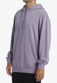 Felpa viola con tasca a canguro, cappuccio con cordino, polsini a coste e logo ricamato sul petto. Materiale in morbido misto cotone.