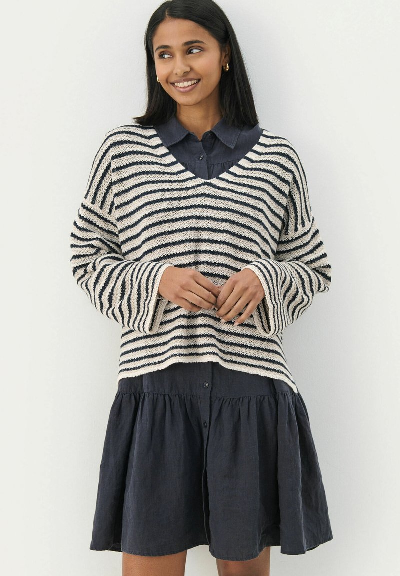 Strikket stribet sweater i creme og marineblå med v-hals og brede ærmer, lagt over en mørk knap-op kjole med en udsvajet nederdel.