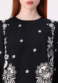 Schwarzes Oberteil aus Stoff mit aufwendigen weißen Blumenmustern und kleinen dekorativen Motiven, mit Rundhalsausschnitt und Puffärmeln.