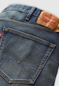 Siniset farkut, joissa on oranssit tikit takataskussa, nahkainen Levi's-bränditunnus ja pieni punainen Levi's-tagi sivusaumassa.