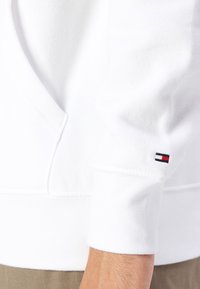 Felpa bianca con tessuto morbido, polsini a coste e un piccolo logo rosso, bianco e blu sulla manica.