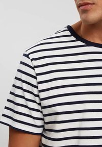 Koszulka w paski w granatowo-białe poziome paski, z krótkimi rękawami i okrągłym dekoltem. Miękka tkanina o gładkiej fakturze i kontrastowym wykończeniu.