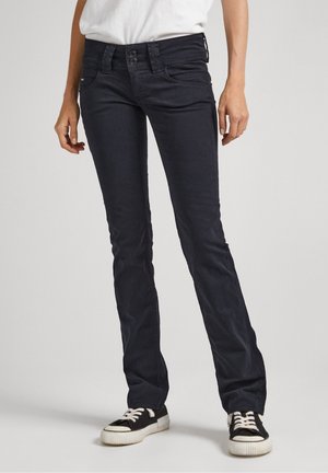 Jeans oscuros de pierna recta, hechos de denim con una textura suave. Con cierre de doble botón y bolsillos laterales. Combinados con zapatillas negras.