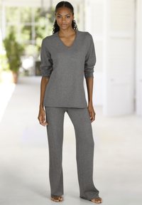 Pelēkas kokvilnas mājas apģērba komplekts, kas ietver garām piedurknēm V veida kakla topu un platu piegriezumu bikses, abiem ir mīksta tekstūra un brīva piegriezuma forma.