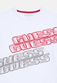 T-shirt en coton biologique blanc avec des graphismes de texte en 3D rouges et gris. Encolure ronde avec une bordure contrastante rouge.