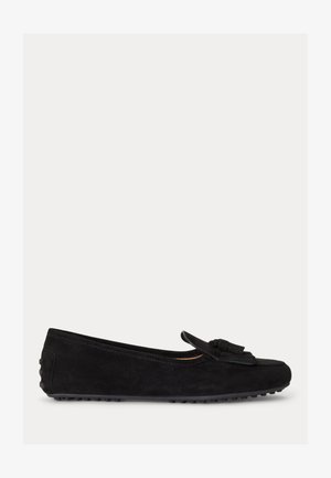 Mocassin en daim noir avec détail à pompon sur le dessus et semelle en caoutchouc texturée, vue de côté sur fond uni.