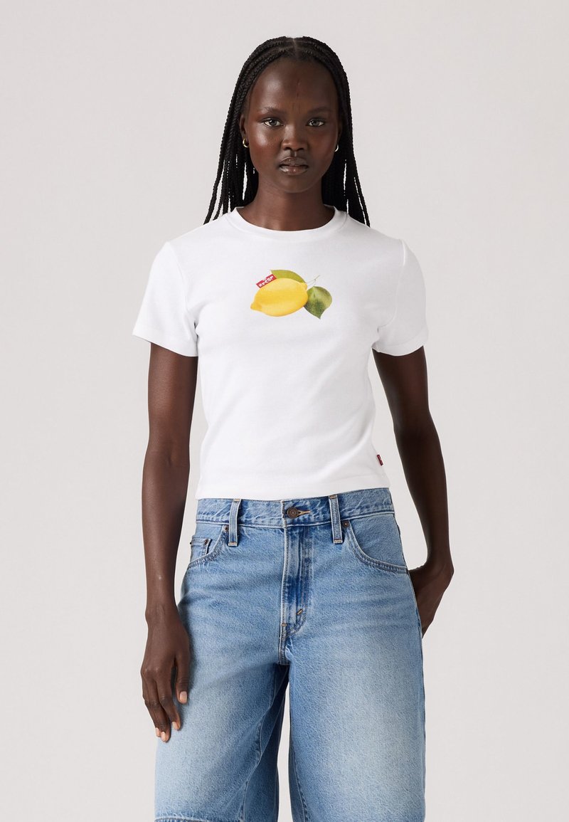 T-shirt alb din bumbac, cu un grafic de lămâie pe piept și o etichetă cu logo-ul Levi's. Asortat cu pantaloni scurți din denim de culoare albastru deschis.