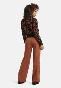 Black sweater with leopard print in brown tones, paired with high-waisted, wide-leg pants in rust-colored faux suede. Chunky black heels.