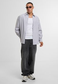 Grå stribet skjorte med knapper, hvid tank top under, parret med løse sorte jeans og sølv sneakers. Struktureret stof, afslappet pasform.