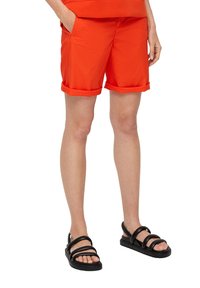Oranje shorts met opgerolde zomen, voorzien van zijzakken en een losse pasvorm, gecombineerd met zwarte strappy sandalen.