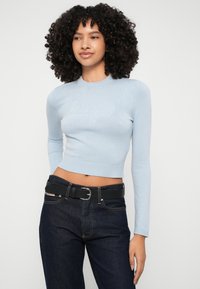 Ανοιχτό μπλε κοντό πουλόβερ με μακριά μανίκια και ριγωτή υφή. Διαθέτει μια διακριτική σχεδίαση λογότυπου στο στήθος, συνδυασμένο με σκούρα τζιν και μαύρη ζώνη.