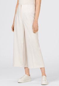 Krämfärgade byxor med vida ben i ett mjukt tyg, med framsydda veck, hög midja och en strukturerad design. Matchas med vita sneakers.