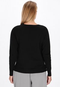 Pulover negru cu guler rotund, mâneci lungi tip raglan și un tiv inferior ușor ajustat. Materialul pare a fi tricotat și moale.