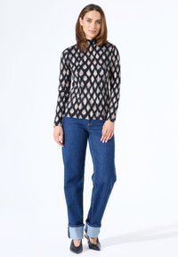 Zwarte top met lange mouwen en beige ikatpatroon, hoge halslijn. Gecombineerd met hoge taille blauwe spijkerbroek, opgerolde manchetten en zwarte hakken.