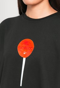 Čierne bavlnené tričko s lesklou grafikou oranžovej cukrovej tyčinky a s textom "Fiorucci", ktorý je výrazne umiestnený na prednej strane.