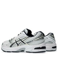 Valkoiset urheilukengät, joissa on verkkopäällinen, mustat ja hopeiset yksityiskohdat, pyöreä kärki, pehmustettu nilkkapanta ja paksu kumipohja. Karhea pinta pidon parantamiseksi.