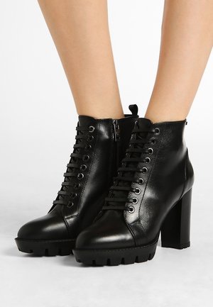 Bottines en cuir noir avec un talon épais, présentant un avant à lacets, une fermeture éclair et des semelles texturées pour une meilleure adhérence.