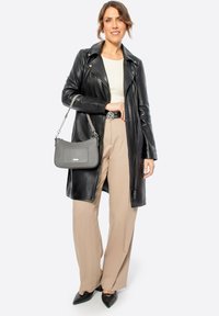 Abrigo largo de cuero negro, pantalones de pierna ancha beige, blusa crema, bolso gris texturizado con cadena y zapatos negros de punta. Accesorios de metal plateado.