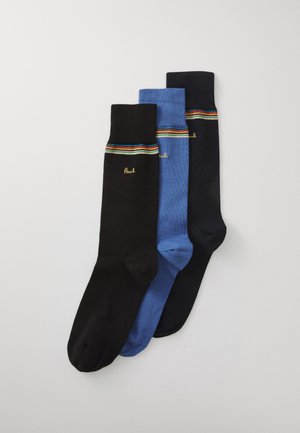 Tre par sokker: en svart, en lys blå, en mørk blå. Hver sokk har et stripete mønster på toppen og en logo i gul.