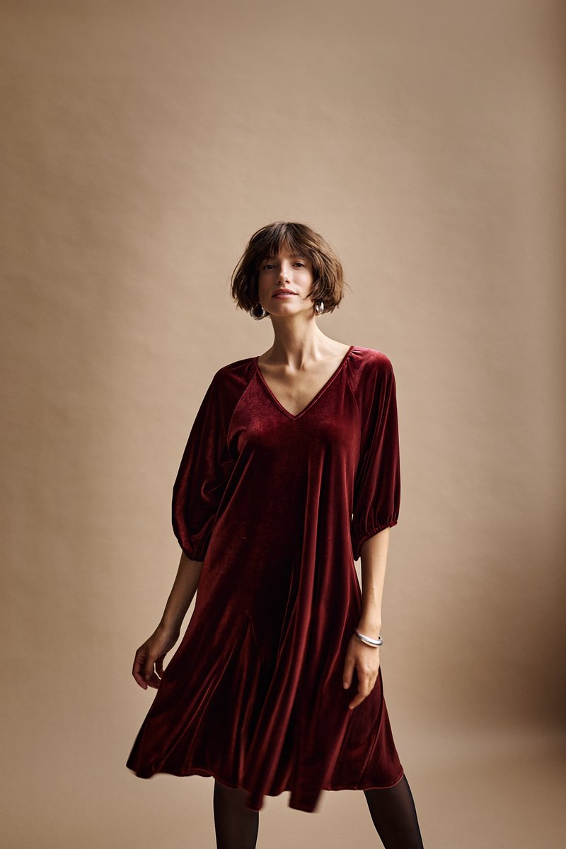 Burgunderfarbenes Samtkleid mit V-Ausschnitt, kurzen Puffärmeln und schwingender A-Linie. Glatte Textur und knielanges Design.