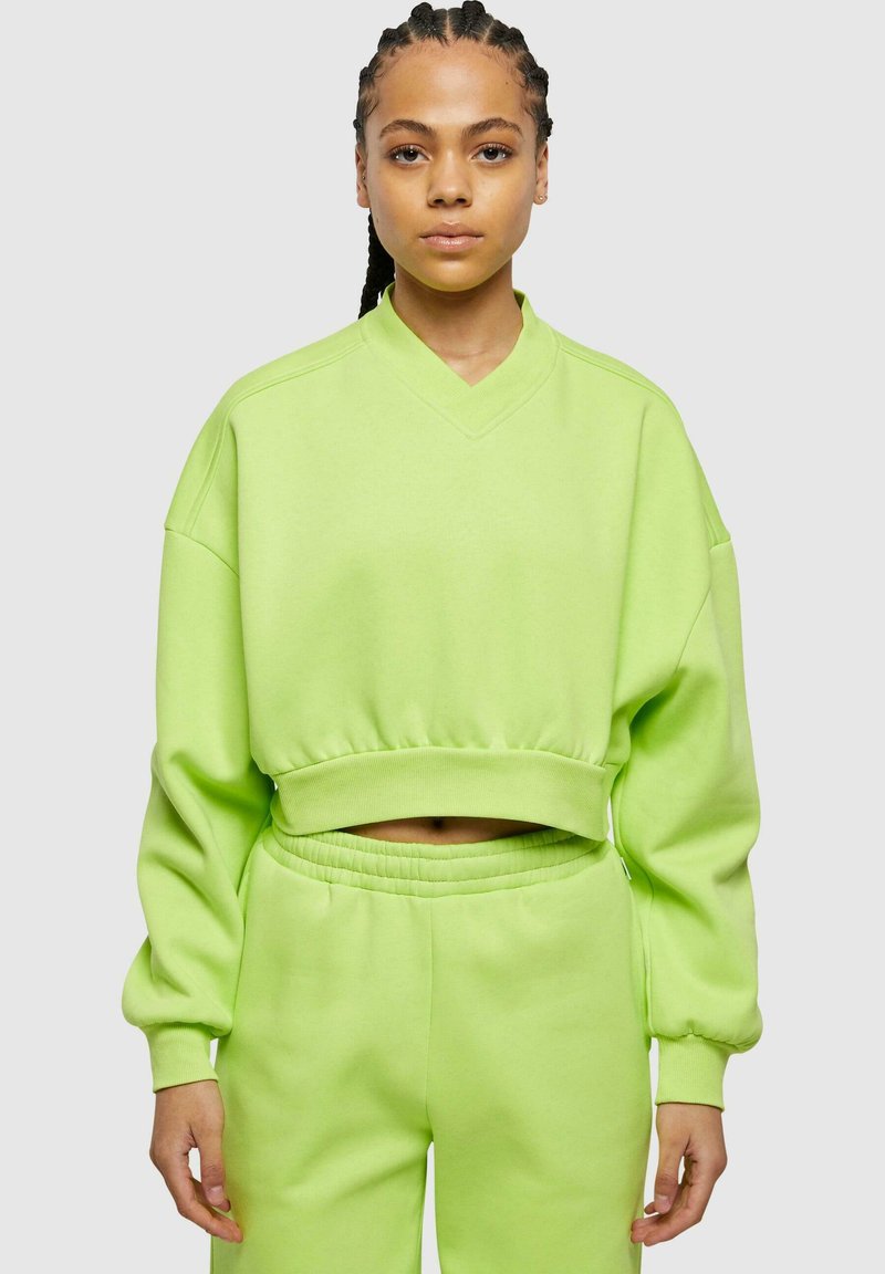 Felpa verde neon corta con scollo a V, maniche ampie e orlo elastico. Abbinata a pantaloni della tuta a vita alta coordonati.
