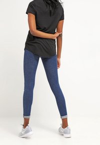 Svart T-shirt med kort ärm som kombineras med blå slim-fit jeans. Jeans är uppvikta vid anklarna och kompletteras av grå sportskor.