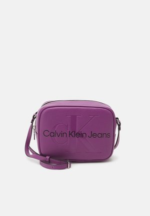 Petit sac bandoulière violet avec une bandoulière réglable, logo "cK" en relief à l'avant et texte "Calvin Klein Jeans" en noir.
