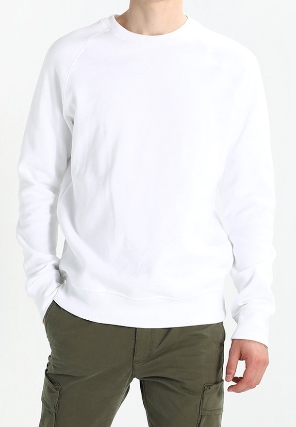 Personne portant un sweat-shirt blanc uni à manches longues et un pantalon cargo vert olive, debout avec une main dans la poche sur un fond blanc.