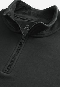 Pullover nero con colletto a mezza zip, realizzato in materiale morbido. Presenta un colletto a coste e un'etichetta con il marchio all'interno.
