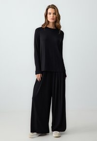 Zwarte lange mouwen top en brede broek set, gemaakt van zachte stof. De broek heeft een geplooid design en wordt gedragen met lichtgekleurde sneakers.