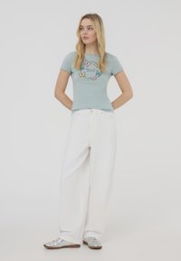 T-shirt aderente azzurro chiaro con motivo a farfalla, abbinato a pantaloni bianchi larghi e sneakers argento; design semplice, tessuto morbido, vestibilità comoda.