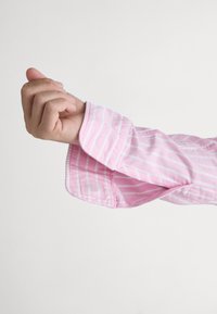 Light pink shirt with white stripes, detailed cuff visible, soft fabric texture, and a slightly folded sleeve, showcasing tailored design.