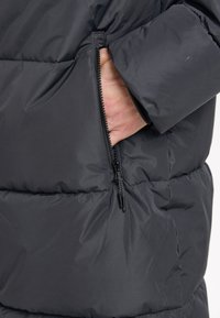 Doudoune noire au fini mat, avec une poche zippée sur le côté. Le tissu est lisse, avec un design matelassé.