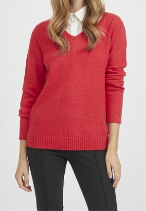 Roter Wollpullover mit V-Ausschnitt, gerippten Bündchen und Saum, kombiniert mit einem weißen Hemd mit Kragen, aus weichem, strukturiertem Stoff.