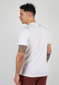 T-shirt blanc à manches courtes en coton, présentant un col rond à côtes et une petite étiquette logo au dos près de l'épaule.