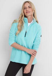 Light teal fleece pullover with a half-zip collar, long sleeves, and a black logo patch on the left arm. Soft, textured material.
