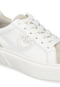 Zapatilla blanca de cuero con un acento de ante beige, cierre de cordones, suela de goma texturizada y detalle destacado del logo en el lateral.