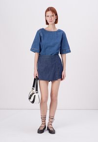 Denimový outfit pozostávajúci z modrého krátkeho rukáva a sukne typu wraparound. Obsahuje tiež čierne šnurovacie baleríny a malú bielu kabelku.