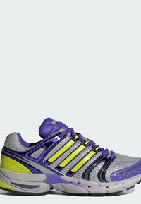 Chaussure de sport violette et grise avec tige en mesh, accents métalliques, bandes réfléchissantes jaunes et semelle rembourrée.