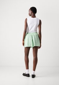 Shorts verzi cu dungi albe, cu talie elastică, realizate dintr-un material ușor, cu o croială lejeră și buzunare laterale. Se pot asorta cu un top alb.
