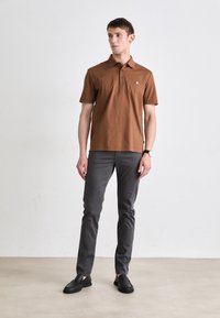 Barna pólóing rövid ujjakkal és három gombbal, szürke, slim fit nadrággal és fekete slip-on cipővel párosítva.