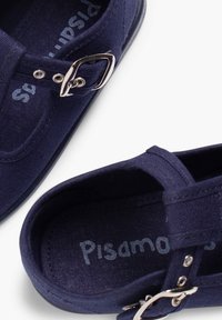 Granatowy materiałowy but z okrągłym noskiem, pojedynczym paskiem i srebrną metalową klamrą. Wewnątrz na materiale znajduje się napis "Pisamonas" w jasnoniebieskim kolorze.