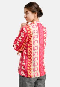 Long-sleeve shirt featuring a multicolored design in pink, peach, and cream with abstract patterns and smooth texture.