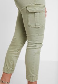 Olivegröna cargo-byxor med uppvikta fållar, med sidofickor och sydda detaljer, tillverkade av en stretchig bomullsmaterialblandning.
