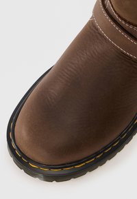 Brune lærstøvel med rund tupp, kontrasterende gul syning langs gummisålen, med en jevn tekstur.