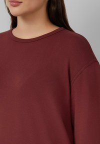 Bordeaux sweatshirt met een ronde hals, verlaagde schoudernaden, zachte textuur en een relaxte pasvorm. Minimalistisch ontwerp zonder patronen.