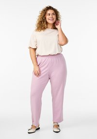 Béžový top s krátkymi rukávmi doplnený svetloružovými nohavicami s elastickým pásom. Model stojí na jednoduchom pozadí, predvádzajúc uvoľnený strih a doplnkové farby.